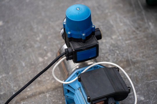 Electric water pressure booster pump with automatic electronic controller unit installed on top, detail of domestic or garden water supply system equipment on concrete ground.