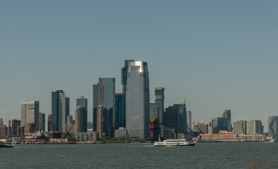 Obraz premium Scenic Jersey City vista from a boat in summer with sun reflecting at the top of a skyscraper, New Jersey