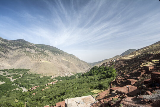 View of the traditional Berber village of Tizi Oussem in the High Atlas Mountains with terraced fields and lush greenery under a wispy blue sky Tizi Oussem, Marrakech-Safi, Morocco.