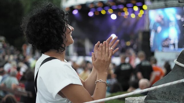 Party woman clapping her hands in front of a crowd. The crowd is watching a performance. The woman is smiling and she is enjoying the show in slow motion