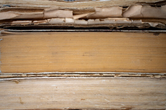 Macro texture of aged yellowed paper pages and worn edges of stacked old antique books, representing an abstract library background, historical archives, and literature.