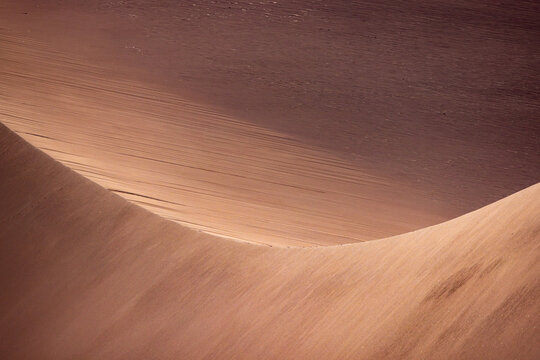 View of the smooth curves and wind-swept textures of the sand dunes in the Valley of the Moon, San Pedro de Atacama, Antofagasta, Chile.