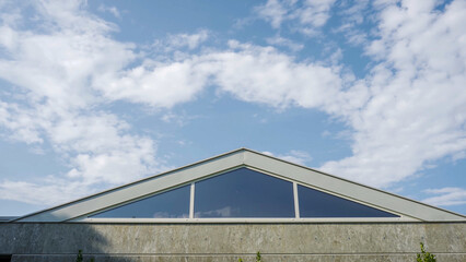 Obraz premium Exterior view of a modern building featuring a large triangular glass window against a cloudy blue sky