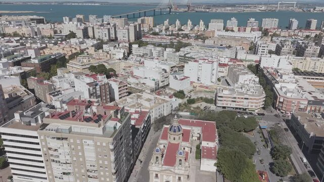 Aerial view of San Jose Church in Cadiz, Spain. Cinematic drone shot of the historic Neoclassical parish and surrounding city streets on a sunny day.