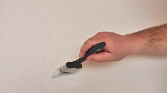 Paintable Wallpaper.Movement of a paintbrush in white paint on a textured wall. Repairing a Wallpapered Wall. A man paints textured wallpaper white using a paintbrush. 4k footage