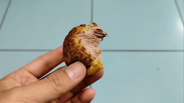 Close-up image of a choux pastry filled with chocolate cream after being bitten into, with creamy chocolate inside.