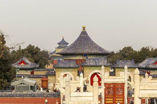 View of the Temple of Heaven complex featuring traditional blue-tiled roofs, red gates, and white marble structures with people walking around Beijing, Beijing, China.