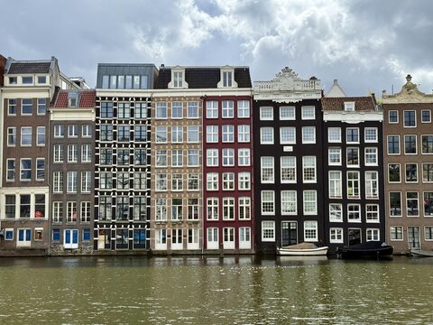View of traditional narrow canal houses with ornate gables and large windows reflecting on the water in Amsterdam, Netherlands.