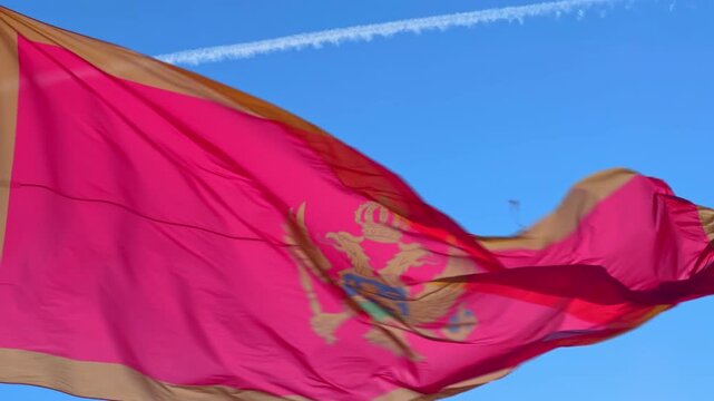 A red and gold Montenegro national flag with double headed eagle waves dramatically in the wind against a clear blue sky creating a powerful patriotic emblem of statehood
