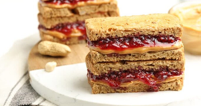 Tasty peanut butter and jelly sandwiches on table, closeup. Camera moving right