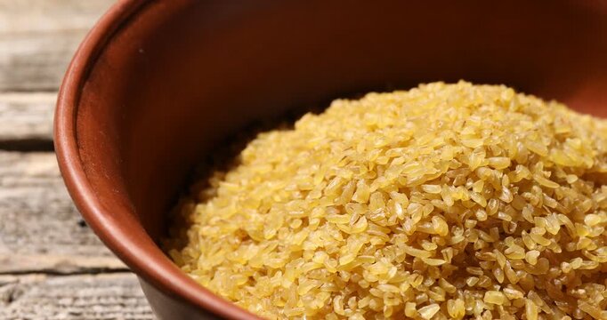 Raw bulgur in bowl on wooden table, closeup. Camera moving right