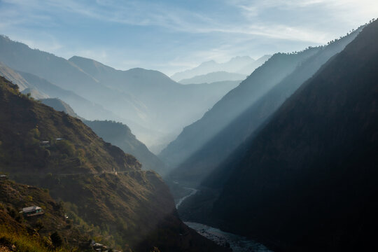 View of sunbeams piercing through the mist in the deep Neelum Valley with a winding river and steep mountain slopes in Arang Kel, Azad Kashmir, Pakistan.