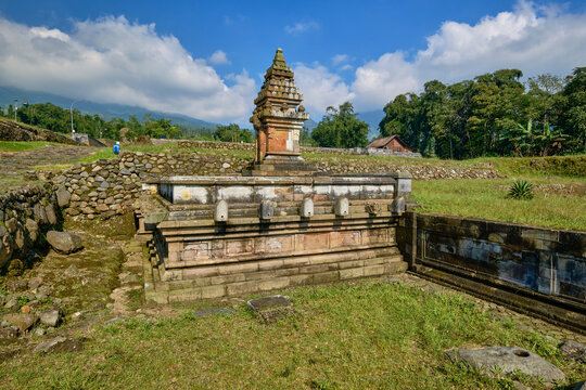 View of the ancient stone temple at Situs Liyangan surrounded by stone walls and lush greenery under a blue sky in Ngadirejo, Central Java, Indonesia.