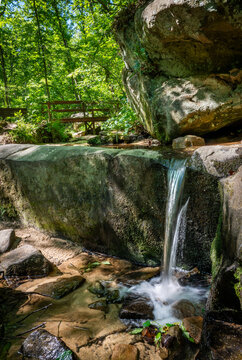 View of a small waterfall cascading over mossy sandstone rocks into a clear pool at Pickle Springs Natural Area surrounded by lush green forest New Offenburg, Missouri, United States.