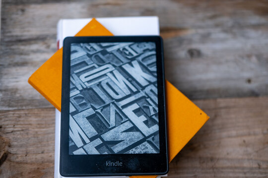 modern Kindle e reader on stack paper books, black e-book reader, digital book Kindle, tablet computer device displaying text electronically, electronic paper technology, reading fiction, text editing
