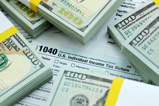 1040 Individual Income tax return form and hundred dollars money bills packs on accountants table