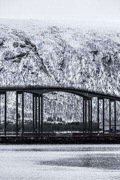 View of the Tromso Bridge with its concrete pillars and arched span against a backdrop of snow-covered mountains Tromso, Troms, Norway.