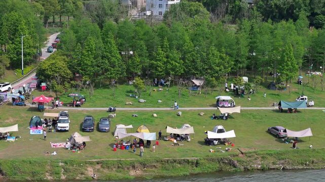 Camping crowds and vehicles on outdoor grasslands along the Xin'an River