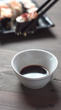 Close up sushi roll dipped in soy sauce with chopsticks on rustic wooden table, Japanese food concept with shallow depth of field.