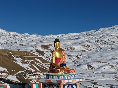 Kaza, India - 28 January 2026: View of the golden Buddha statue in Spiti Valley overlooking snow-covered Himalayan mountains under a clear blue sky.