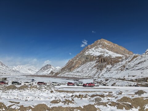 Kaza, India - 28 January 2026: View of a convoy of off-road vehicles parked on a snowy road in the Spiti Valley, surrounded by rugged snow-covered mountains under a clear blue sky.