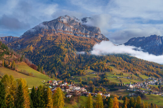 Majestic mountain peak with colorful autumn larch forest and rolling clouds near Colle Santa Lucia, Dolomites, Italy.
