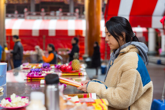 Young woman praying with joss paper at traditional chinese temple