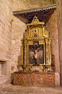 Plasencia, Spain - 03 December 2025: View of the ornate gilded altarpiece with a crucifix inside the Catedral Nueva de Plasencia featuring intricate golden carvings and stone walls.