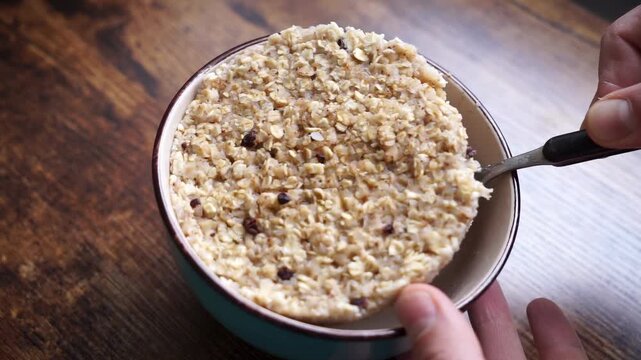 Close-up of failed oatmeal porridge with dry thick texture and compact clump lifted from bowl with spoon. Funny cooking fail, ruined breakfast, swollen oats, bad consistency.