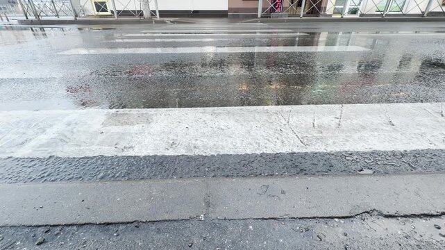 A wet white zebra crosswalk stretches across a broad asphalt street after a storm. The gleaming water reflects the empty city surroundings, evoking a quiet, peaceful, and lonely mood.