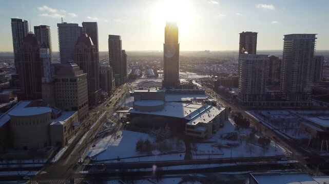 Aerial over a mall and Canadian flag in Mississauga, Ontario, Canada. City centre, city hall and several residential condominium towers. Flying into the sun with lens flare on a winter December day.