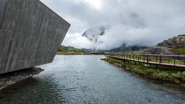 Andalsnes, Norway - 23 June 2024: View of the Trollstigen visitor center and wooden walkway by a mountain lake under a cloudy sky.