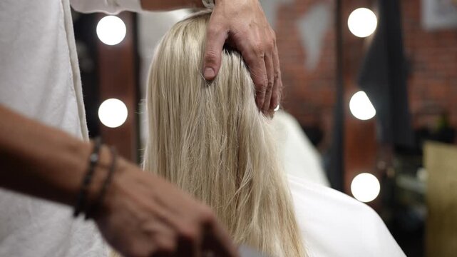 Professional male hairstylist combing a woman's long blonde hair in a beauty salon. The client is receiving hair treatment and styling