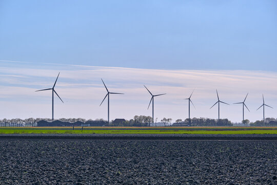 Middenmeer, Netherlands - 14 April 2026: View of Vattenfall wind turbines in the Wieringermeer standing in a row across flat agricultural fields under a clear blue sky.