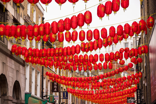 London, United Kingdom - 12 May 2025: View of traditional red Chinese lanterns hanging across the streets of Chinatown between historic brick buildings under an overcast sky.