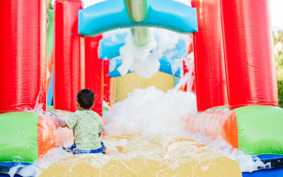 Ni&ntilde;o jugando en resbaladero inflable acu&aacute;tico con espuma y colores vibrantes en parque recreativo