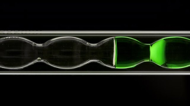 Air bubbles swirl through green transparent liquid as it fills and drains from vertically installed bulb lab condenser over dark bg | Bamboo water ingredient visualization concept