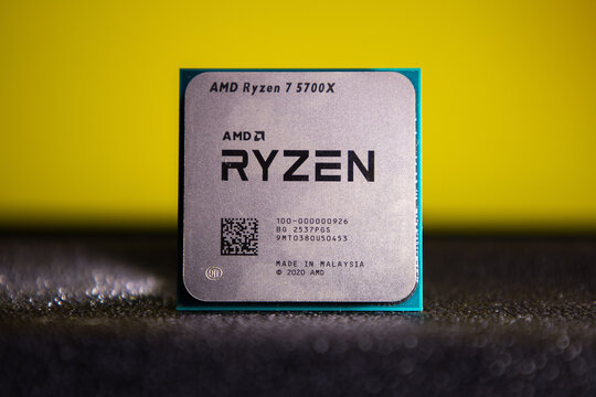 AMD Ryzen 5700X desktop CPU shown in vibrant close-up on a textured surface with a bright yellow gradient backdrop. This microprocessor, manufactured by AMD in Malaysia, features clear branding and mo
