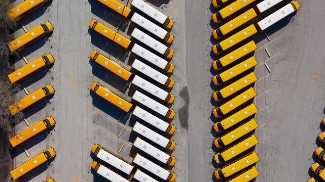 Aerial view of rows of white and yellow school buses in parking lot.