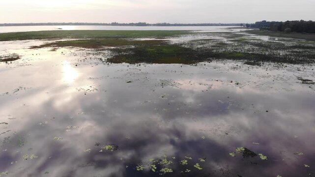 Aerial view of a serene wetland landscape with calm water and grassy areas at sunset.