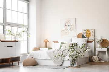 Fototapeta premium Interior of stylish bedroom with bed, commode and vases of blooming tree branches