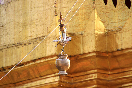 Golden hti (umbrella) with dragon-shaped finial and water pot pouring holy water over , Thai temple.