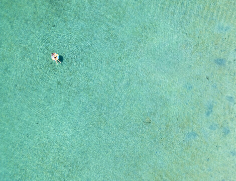 Aerial view of a person relaxing on an inflatable ring in the crystal clear turquoise waters of the Caribbean Sea in Guanaja, Bay Islands Department, Honduras.