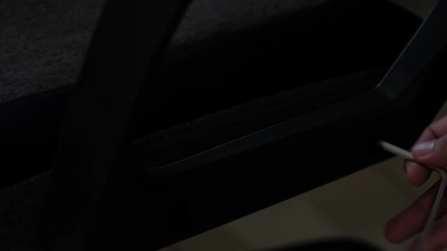 Close-up static shot of hands using an allen wrench to adjust a gaming chair armrest during indoor furniture assembly