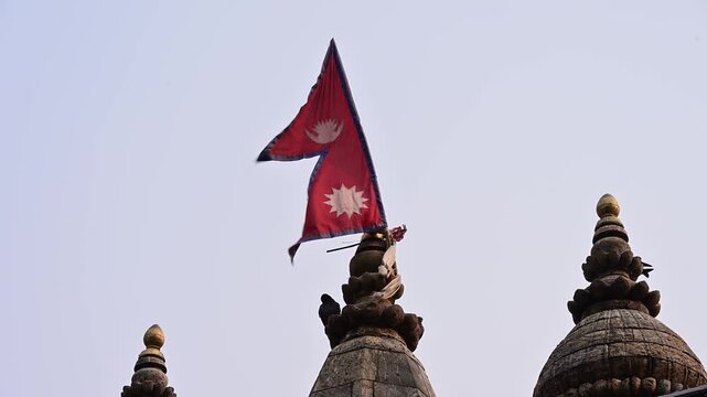 Nepali flag on ancient temple in Kathmandu. The shape of the flag is said to represent the Nepalese mountains. The sun and moon represent the hope that the country will last as long as the sun and moo