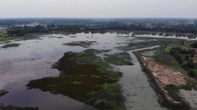Aerial view of the Huay Saneng reservoir area with green algae on the water surface and lush vegetation in Surin, Thailand.