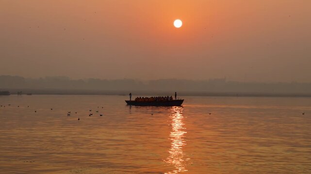 silhouette passenger boat sailing across calm ganges river during dramatic varanasi ghat sunrise
