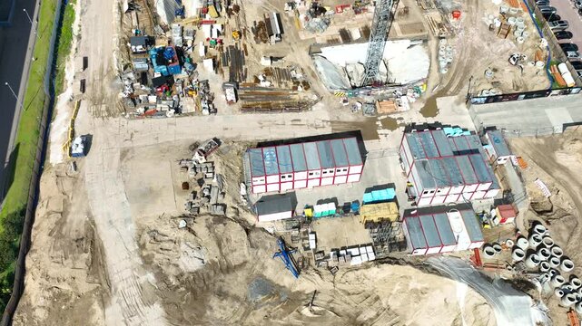 A cinematic highangle shot showing a busy construction site with modular offices, heavy machinery, and foundation work in Gdynia, Poland.