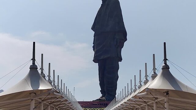 Tilt-down from Statue of Unity silhouette to tensile canopy visitor structures below, revealing human scale. Ideal for landmark docs, heritage films, and India tourism content.