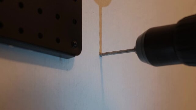 Close-up static shot of a power drill creating a hole in a concrete wall during indoor pegboard installation work